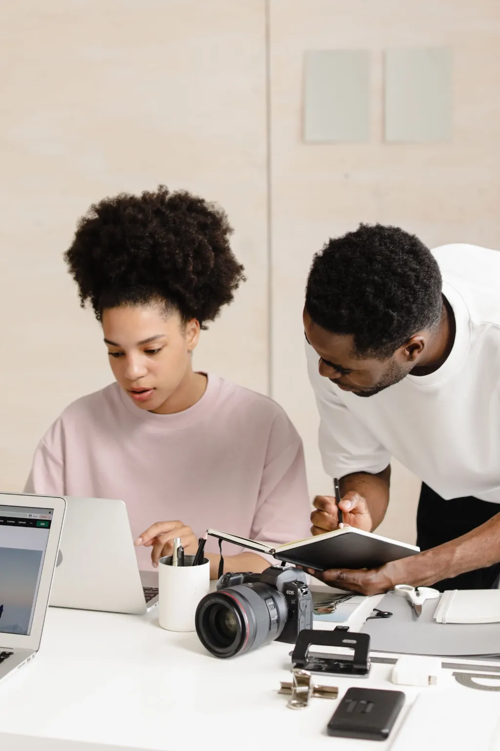 Two content creators review work at a desk with laptops and a camera.